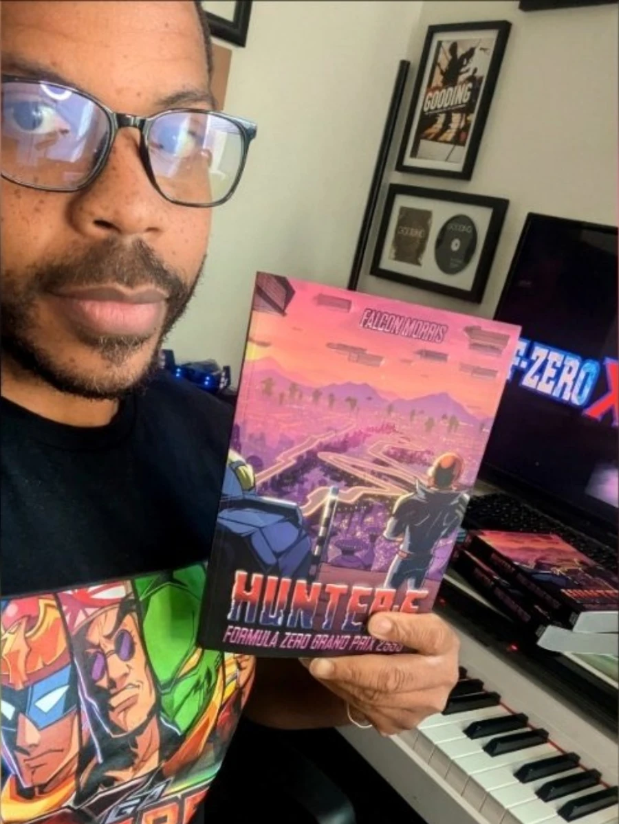 Falcon Morris holding his HUNTER-F novel beside a keyboard.